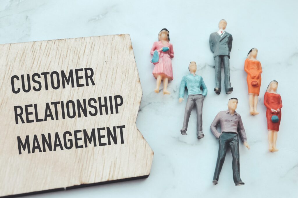 Image of miniature dolls arranged on a countertop with a wooden board displaying 'Customer Relationship Management.' This image illustrates a CRM blog.